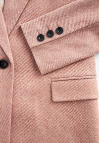 Světle růžový strukturovaný blejzr s klopou, třemi černými knoflíky na rukávu a jednou náprsní kapsou.