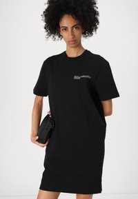 Svart oversize t-shirt klänning med korta ärmar och rund halsringning, med ett broderat logotyp på bröstet och en enfärgad textur.