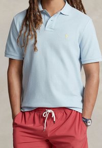 Ljusblå kortärmad polo med en texturerad tyg och ett litet gult emblem. I kombination med röda shorts med resår i midjan.