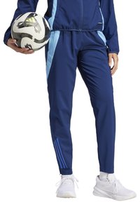 Marineblauwe sportieve trainingsbroek met lichtblauwe zijpanelen, slim fit, elastische tailleband en drie blauwe strepen bij de enkels. Houdt een voetbal vast.