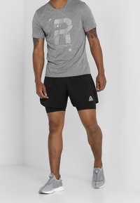 Šedé sportovní tričko s předním potiskem, černé šortky s logem a šedé tenisky s prodyšnými detaily a polstrovanou podrážkou.