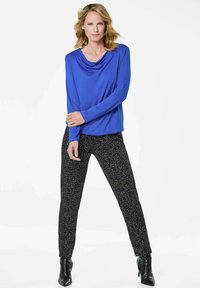 Blaues Longsleeve-Oberteil mit Schalkragen, kombiniert mit schwarzen texturierten Hosen mit einem mehrfarbigen Sprenkelmuster. Schwarze ankle boots mit Absatz.