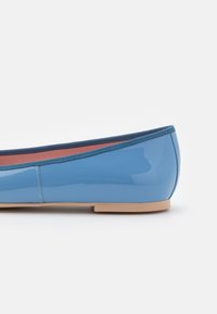 Niebieskie baleriny z lakierowanej skóry, z okrągłym noskiem, wąską beżową podeszwą i kontrastowym niebieskim elastycznym wykończeniem wzdłuż otworu.