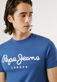 Tricou bleu cu mânecă scurtă, din bumbac, cu decolteu rotund, având un imprimeu mare alb cu textul „Pepe Jeans LONDON” pe piept.