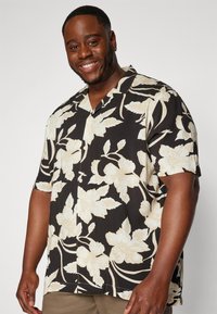 Camisa de manga corta negra con un patrón floral blanco, delante abotonada y de corte relajado. Tejido suave con una textura lisa.