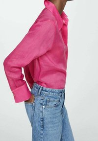 Chemise en lin rose à boutons, avec col et manches longues, associée à un jean en denim bleu clair taille haute avec une coupe classique.