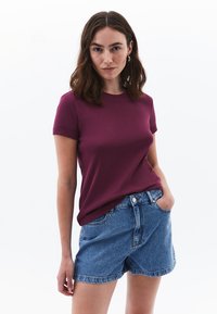 T-shirt girocollo color bordeaux con maniche corte arrotolate, abbinato a pantaloni shorts in denim a vita alta. Tessuto morbido e vestibilità casual.