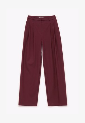 Bordeauxkleurige wijde broek met een gladde textuur, geplooide voorkant en een middelhoog taille. Ontworpen met subtiele stiksels en riemlussen.