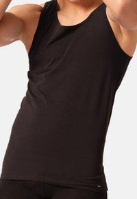Sort tanktop lavet af glat, strækbart stof; ærmeløs design med en rund halsudskæring og en tætsiddende pasform. Diskret logo-detalje ved kanten.