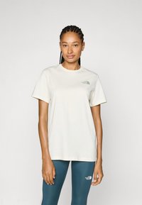 Camiseta de manga corta color crema hecha de una tela suave, con un pequeño logo verde en el lado izquierdo del pecho. Combinada con legging color teal.