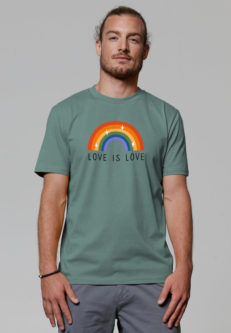T-shirt en coton vert à manches courtes, avec un design de rainbow multicolore et le texte "L'AMOUR EST UN AMOUR" en noir en dessous.