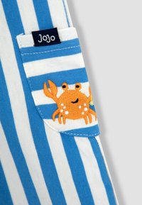 Modrá a biela pruhovaná tkanina s vreckom, na ktorom je vyšitý oranžový krab, a štítkom s nápisom "Jojo." Mäkká bavlnená textúra.