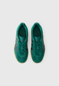 Zeleni semiš supergi z črnimi črtami, zaobljenim prstom, oblazinjenim ovratnikom in gumijastim podplatom v barvi gume, z ujemajočimi se vezalkami in logotipskimi poudarki.