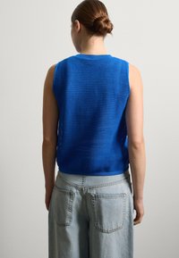 Blaues ärmelloses Strickoberteil mit strukturierten Mustern und rundem Halsausschnitt, kombiniert mit hochgeschnittenen hellblauen Jeans aus Denim mit Gesäßtaschen.