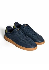 Zapatillas de cuero azul marino con acabado texturizado, que cuentan con una suela de goma, punta redonda y acentos verdes contrastantes en el talón y los ojales.