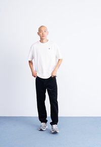 Tricou alb cu mânecă scurtă și un mic logo, asortat cu pantaloni din catifea groasă negri și adidași gri. Design simplu și croială lejeră.