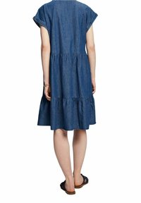 Denim dress with short sleeves, tiered ruffle hem, and back keyhole detail. Worn with flat sandals, showcasing a casual fit and light texture.