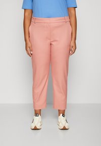  Lichtroze cropped broeken met een gladde textuur en riemlussen, gecombineerd met een blauwe shirt met korte mouwen en witte sneakers.