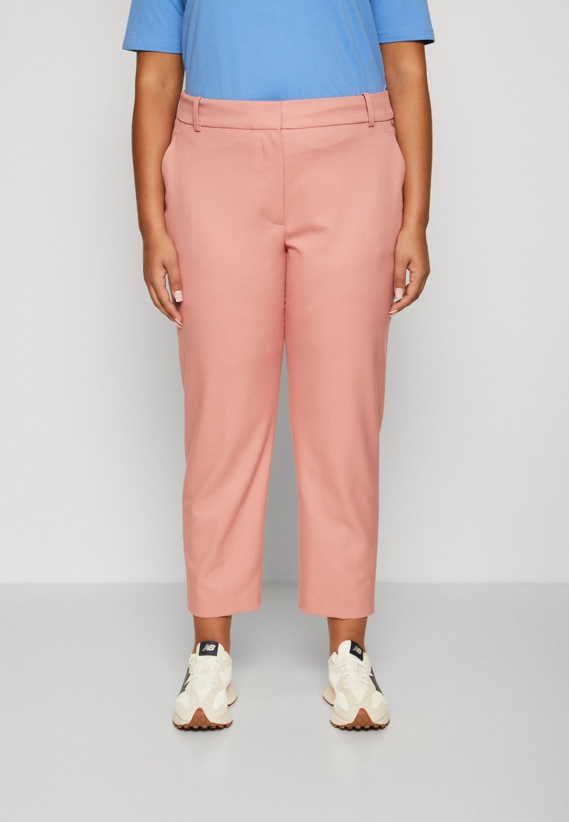  Lichtroze cropped broeken met een gladde textuur en riemlussen, gecombineerd met een blauwe shirt met korte mouwen en witte sneakers.