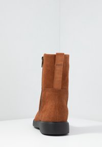 Bruin suède enkellaars met een zijrits, contrasterende stiksels en een gestructureerde zwarte rubberen zool. Versterkte tab bij de hak voor eenvoudig aan- en uittrekken.