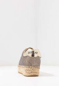 Sneaker en tissu tissé gris avec un talon doré métallisé, semelle en corde de jute et détails de couture blanche. Présente un logo sur le talon.