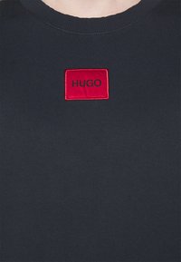 Felpa nera in cotone con un'etichetta rettangolare rossa su cui è ricamato "HUGO" in nero. Collo rotondo classico e colletto a coste.