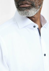 Witte collared shirt met een textuurafwerking, met een contrasterende marineblauwe binnenrand en een donker knoopsluiting.