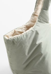 Sac fourre-tout vert clair rembourré avec un extérieur texturé et une doublure beige, présentant un haut arrondi et une large bandoulière pour un transport facile.