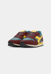 Ténis multicoloridos com camurça burgundy, malha teal e detalhes amarelos. Ponta arredondada, design de atacadores plano e sola de borracha texturizada.
