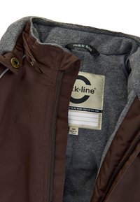 Chaqueta de tejido exterior marrón con forro de forro polar gris. Cuenta con una cremallera, detalles de botones y una etiqueta que dice "mikk-line" con información de tamaño.
