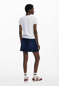 Witte t-shirt met korte mouwen, gecombineerd met een donkere denim minirok. De rok heeft achterzakken en een nette zoom, wat de casual stijl benadrukt.