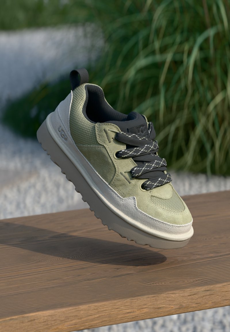 Zöld és szürke sneaker, textúrázott felsőrésszel, fekete fűzőkkel és vastag, világosszürke talppal, természetes háttér előtt bemutatva.