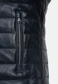 Marineblauwe leren vest met een gewatteerde structuur, een asymmetrische ritszak en horizontale stiksels voor extra stevigheid.