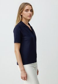 Granatowa koszulka polo z krótkim rękawem, wykonana z miękkiej dzianiny, z klasycznym kołnierzykiem, charakteryzująca się dopasowanym krojem i ściągaczami na rękawach. Połączona z białymi spodniami.