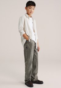 Világos bézs kardigán fehér póló felett, laza, szürke farmernadrággal és sötétbarna cipővel párosítva. Egyszerű dizájn, laza fazon.