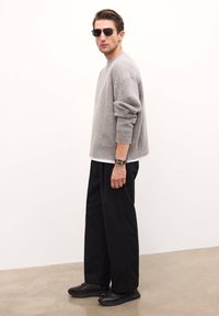 Pulover gri din lână cu manșete cu nervuri, asortat cu pantaloni negri cu croială largă și adidași negri. Stilizat cu ochelari de soare închiși la culoare și o brățară de ceas.