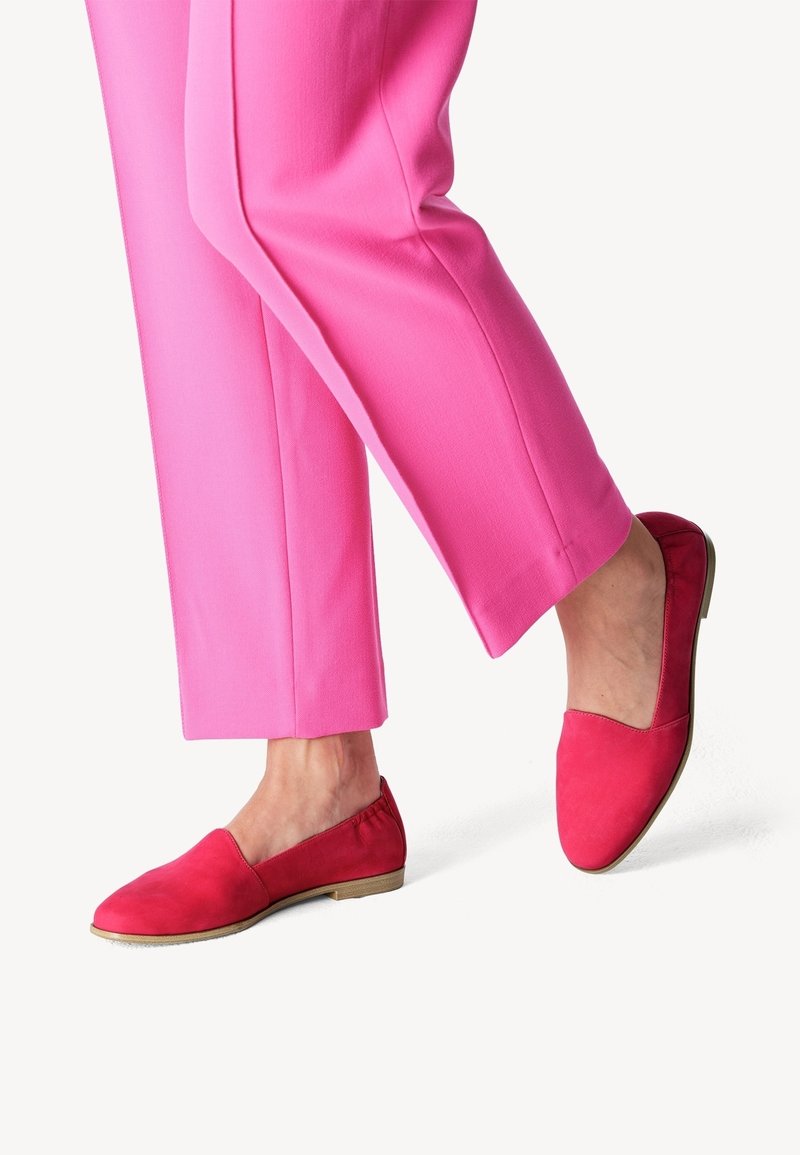 Chaussures en daim rouges sans lacets avec un bout arrondi et un petit talon, assorties à un pantalon sur mesure rose vif, mettant en valeur des textures lisses et des couleurs vibrantes.