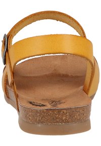 Gelbe Leder-Sandale mit flacher Sohle und zwei verstellbaren Riemen mit einer silbernen Schnalle. Die Basis hat eine Korkstruktur.