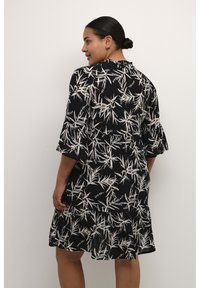 Schwarzes Kleid mit botanischem Druck in Form von weißen Bambusblättern, mit ausgestellten Ärmeln, einem Rüschensaum und einem runden Halsausschnitt. Leichter Stoff.