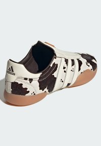 White and black cow-print shoe with a smooth leather upper, rubber outsole, three white stripes, and a slip-on design with a rounded toe.
