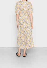 Robe midi florale avec des manches courtes bouffantes, motifs floraux jaunes et pastels sur un fond clair, avec une coupe ample et une longueur cheville.