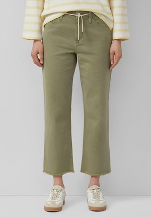 Personne portant un pantalon court vert olive avec des ourlets effilochés, des baskets beige-blanc, et un haut à manches longues rayé jaune et blanc.