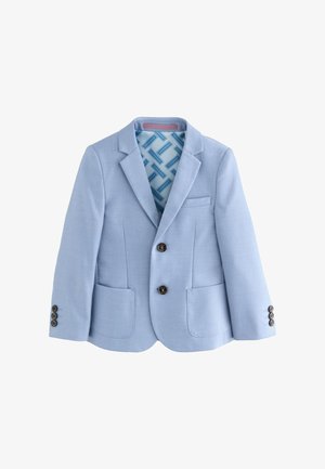 Junger Junge in hellblauem Anzug mit passender Weste und Krawatte, weißem Hemd und marineblauen Sneakers, der mit einer Hand in der Tasche steht.