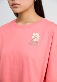 Lichtroze T-shirt met korte mouwen van katoen, voorzien van een bloemenlogo in crèmekleur en groen op de linkerkant van de borst. Eenvoudige ronde hals.