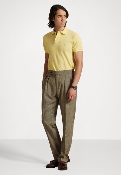 Dzeltena polo krekla ar īsām piedurknēm, kuram ir neliels logotips. Apvienots ar brūnām rūtainām biksēm un brūnām mokasīnām. Klasiskais griezums.