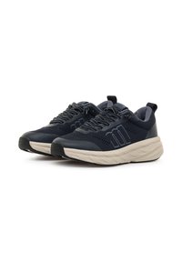 Zapatillas deportivas con parte superior de malla transpirable en un oscuro tono azul marino, entresuela color crema, suela texturizada y diseño de cordones gris. Cuenta con una lengüeta en el talón.