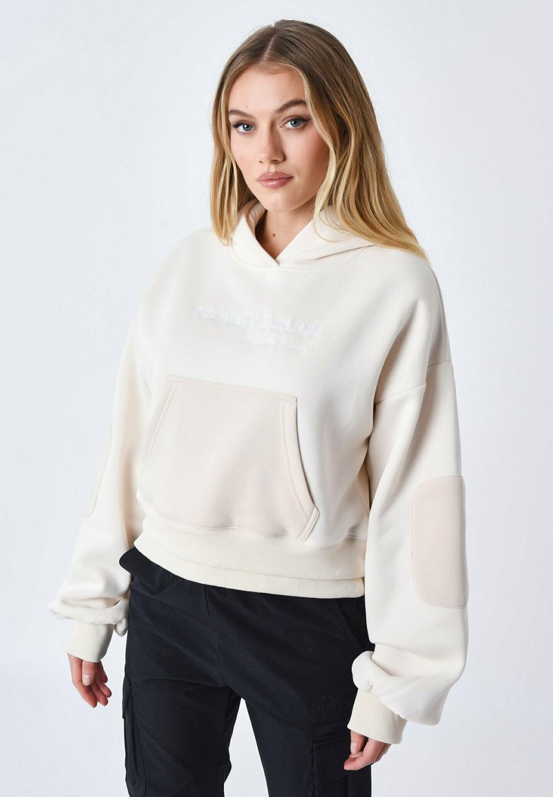Sweatshirt à capuche crème avec une poche avant, un ourlet côtelé et des accents de patch contrastés sur les manches. Tissu doux avec un détail de logo subtil.