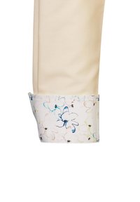 Helle cremefarbene Hosenumschläge mit einem floralen Innenfutter, das leichte Blau-, Gelb- und Rosatöne auf einem weißen Hintergrund zeigt.