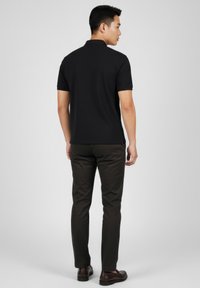 Musta lyhythihainen poolopaita, jossa on kaulus ja sivuhalkiot, yhdistetty ruskeisiin housuihin ja tummaan jalkineisiin. Istuvuus on räätälöity ja nykyaikainen.