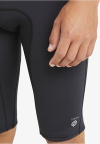 Pantalones cortos de neopreno negro con costuras planas. Presenta un logo y un detalle de tallas en la parte inferior de la pierna izquierda. Textura suave y elástica.